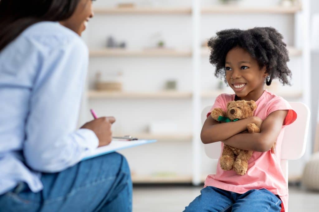 Happy little african american girl at therapy session with psychologist