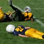 Children’s football players lying on the field after a tackle, illustrating the risks of concussion and the importance of brain injury recovery treatments like IASIS Microcurrent Neurofeedback.