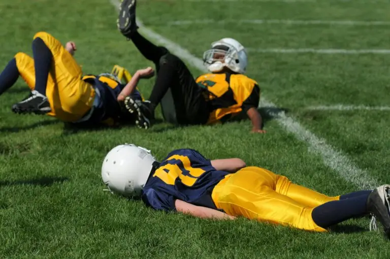 Children’s football players lying on the field after a tackle, illustrating the risks of concussion and the importance of brain injury recovery treatments like IASIS Microcurrent Neurofeedback.