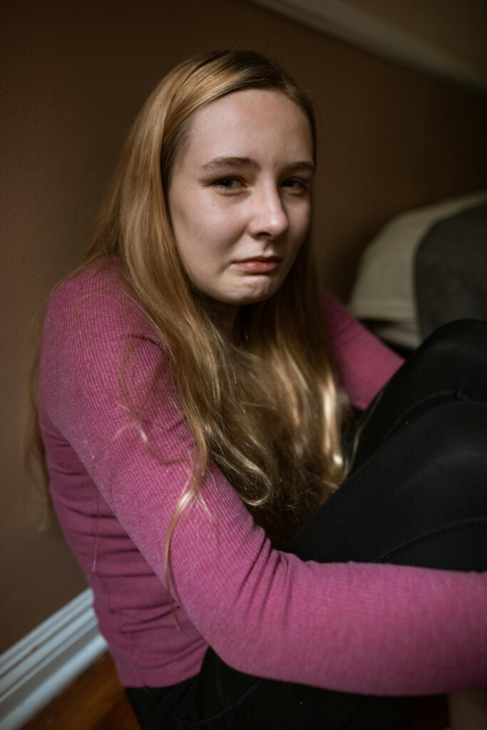 Young woman sitting on the floor with a distressed expression, symbolizing emotional pain and the impact of childhood trauma.