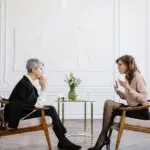 Therapist and client seated face-to-face in a calm counseling office, engaged in a focused mental health therapy session.