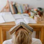A person sitting at a desk with a book resting on their head, symbolizing mental overload, anxiety, and the weight of fear.