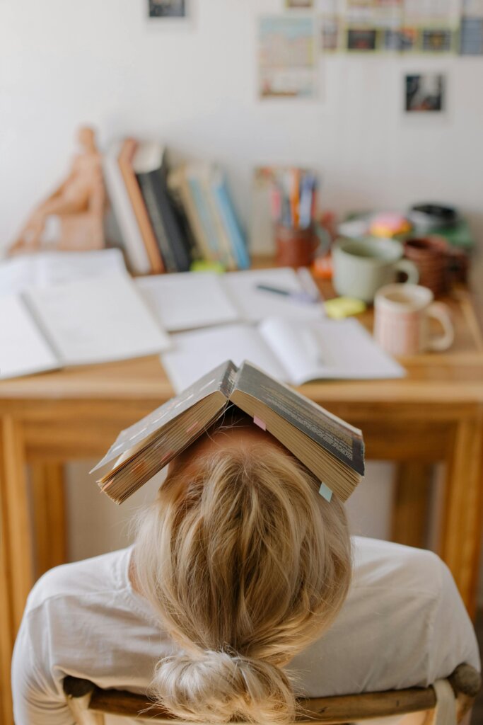 A person sitting at a desk with a book resting on their head, symbolizing mental overload, anxiety, and the weight of fear.