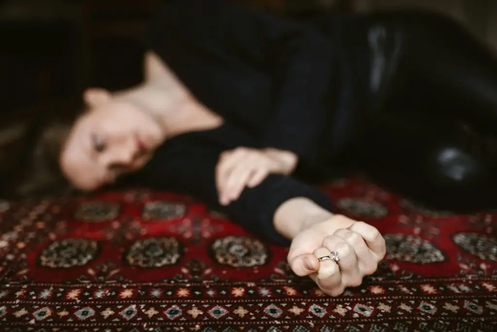 Person lying on a patterned rug holding a ring, illustrating emotional withdrawal and loneliness during depression