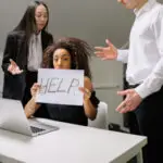 Threat-focused brain and workplace anxiety as a woman holds a help sign while feeling overwhelmed by stress