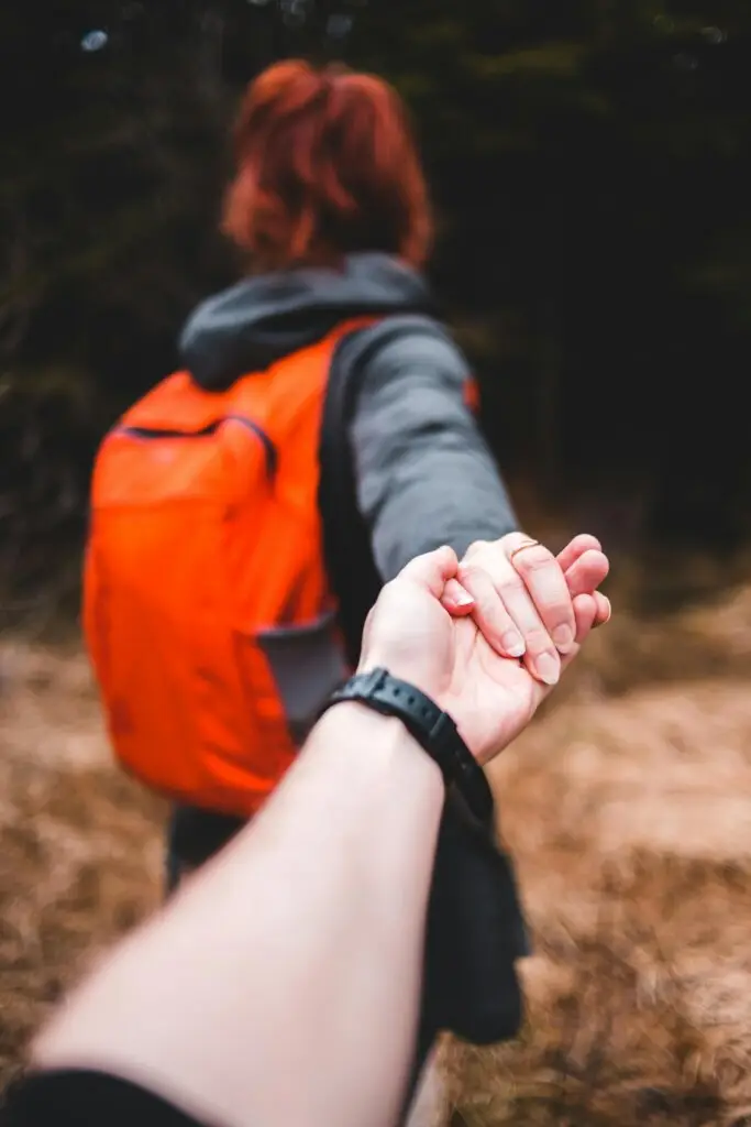 Person holding hands while walking through woods symbolizing trust, emotional support, and the therapeutic healing journey.