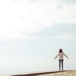 Woman standing with arms open on a path symbolizing freedom with radical responsibility and emotional resilience