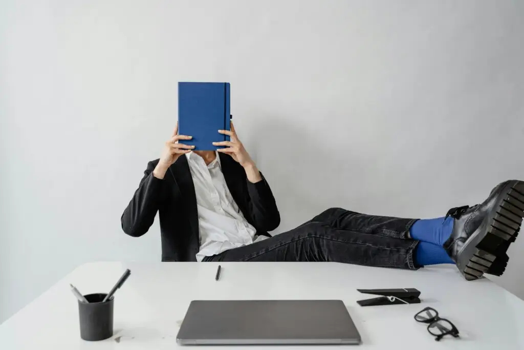 Leader covering face with notebook at desk representing imposter syndrome and workplace anxiety