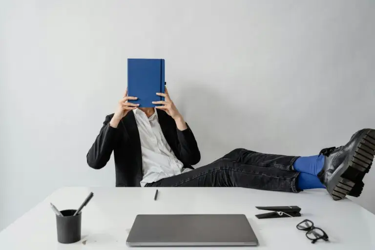 Leader covering face with notebook at desk representing imposter syndrome and workplace anxiety
