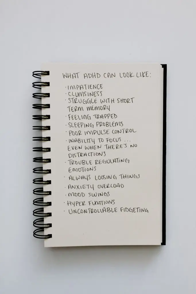 Notebook listing common ADHD symptoms including impulsivity, memory challenges, emotional regulation difficulties, and focus problems.