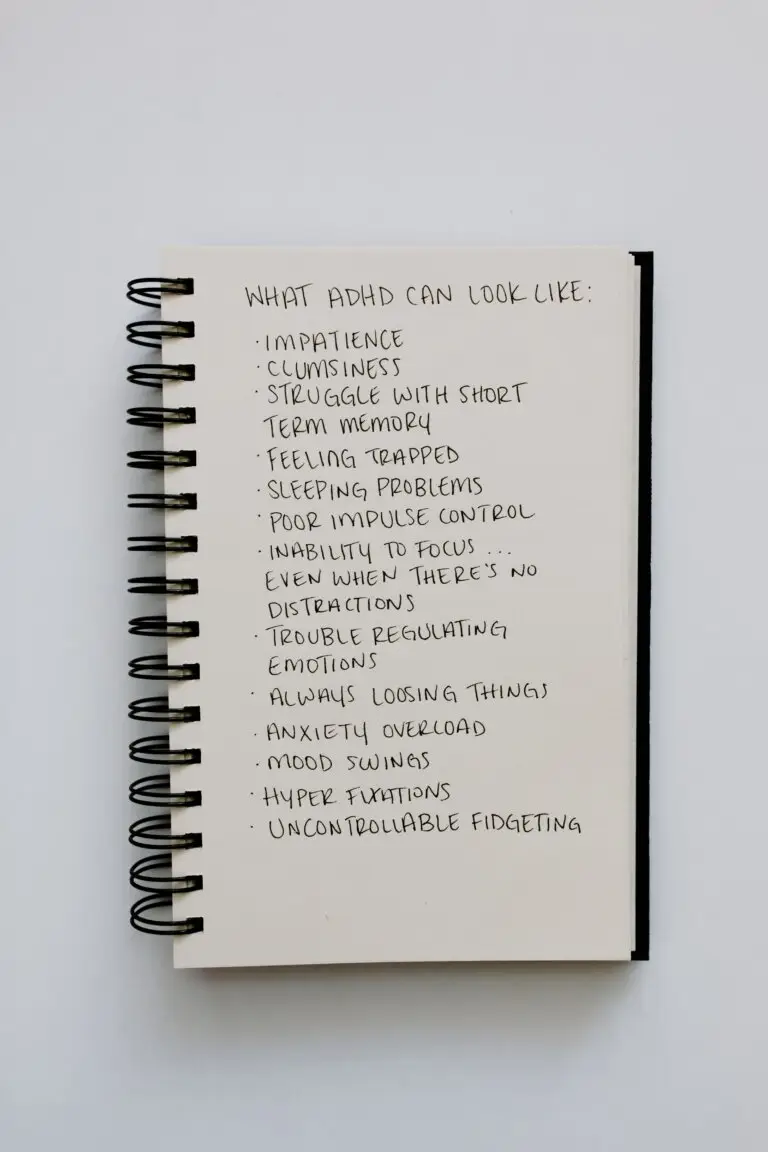 Notebook listing common ADHD symptoms including impulsivity, memory challenges, emotional regulation difficulties, and focus problems.